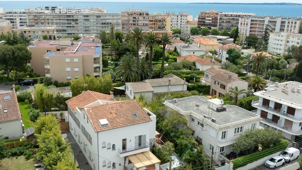 A residential area with multi-story buildings, some with balconies, and a view of the sea in the background.