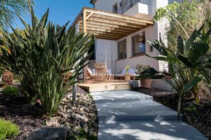 Un espace patio agrémenté d’une pergola en bois, de sièges d’extérieur et de plantes tropicales.