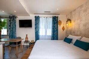 Une chambre d’hôtel moderne avec un grand lit, un bureau avec une chaise, un téléviseur fixé au mur et une fenêtre avec des rideaux bleus.