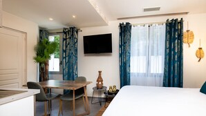 A hotel room with a bed, a dining table with chairs, a TV, and a window with curtains.