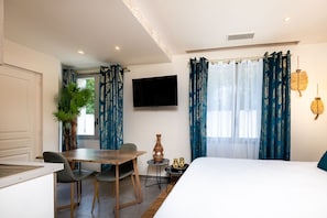 A hotel room with a bed, a dining table with chairs, a TV, and a window with curtains.