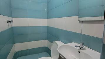 Un baño con azulejos azules y blancos, un inodoro blanco y un lavabo con un cubo de basura rojo.