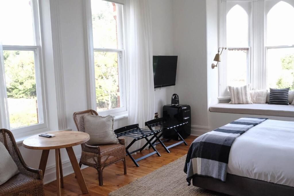 A bedroom with a bed, a TV, a seating area with a table and chairs, and large windows.