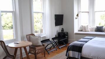 A bedroom with a bed, a TV, a seating area with a table and chairs, and large windows.