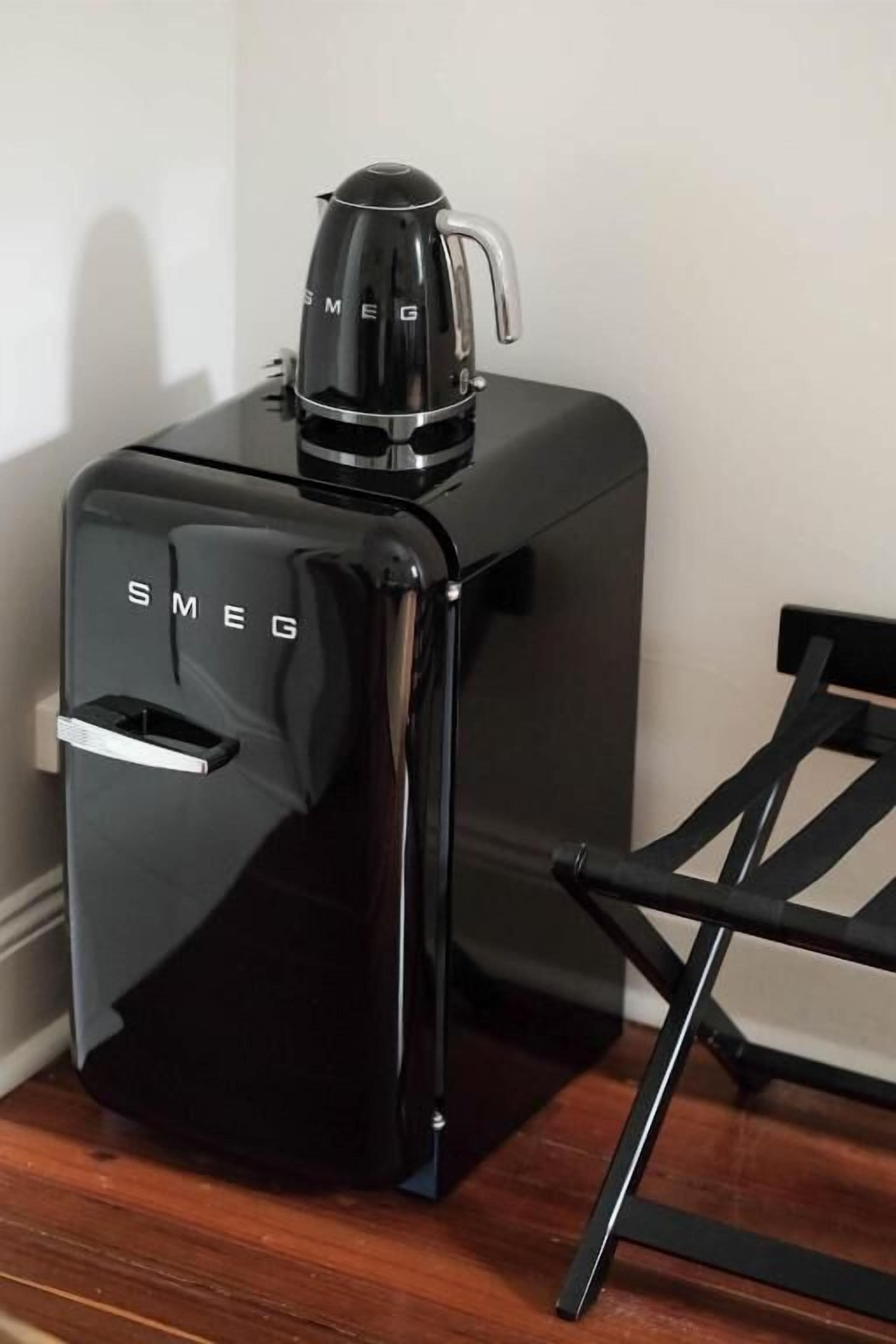 Una máquina de café negra y moderna con un asa y una boquilla, sobre una superficie de madera junto a una silla negra.