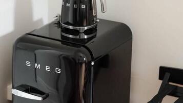 Una máquina de café negra y moderna con un asa y una boquilla, sobre una superficie de madera junto a una silla negra.