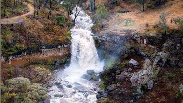A waterfall cascading over rocks in a natural setting with surrounding trees and a dirt path.