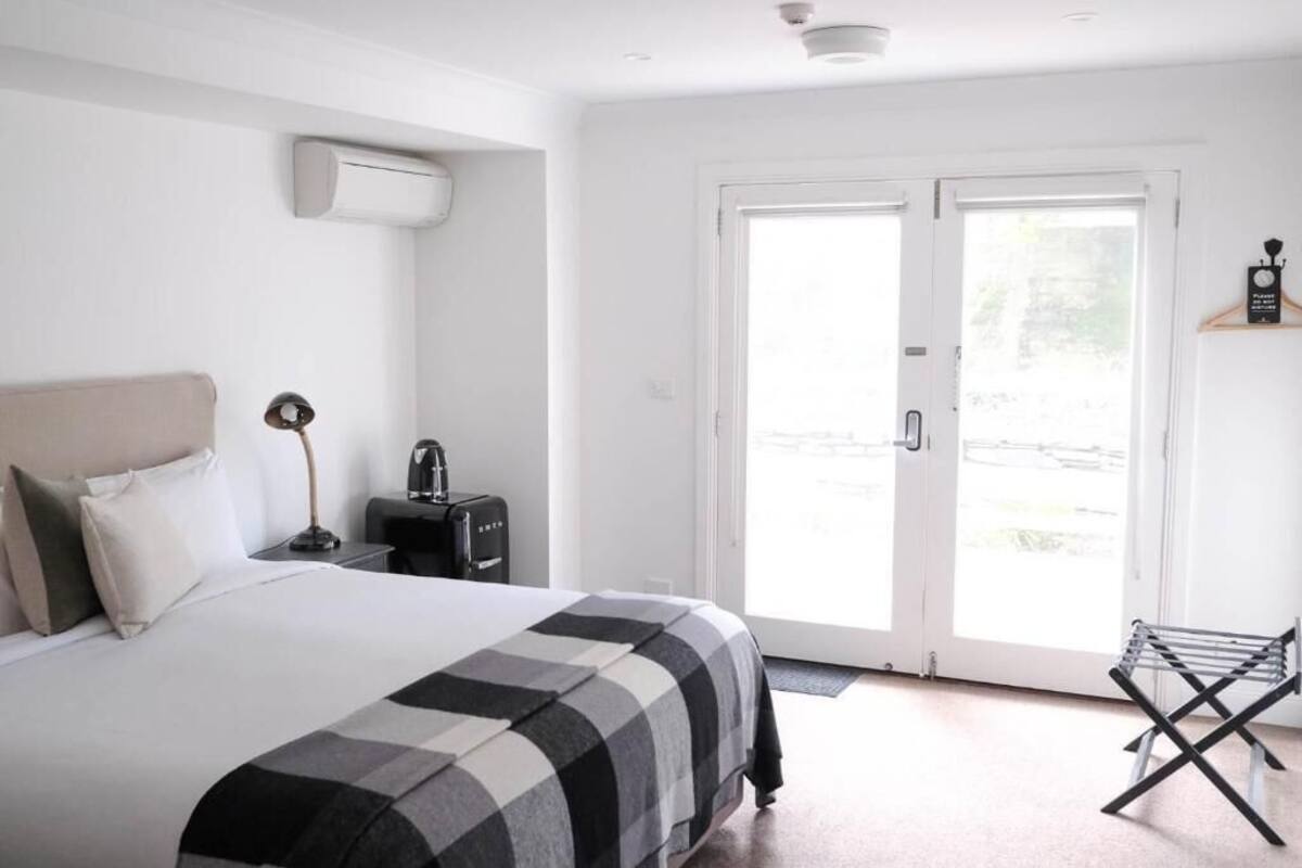 A hotel room with a bed, a desk, a chair, and a door leading to an outdoor area.