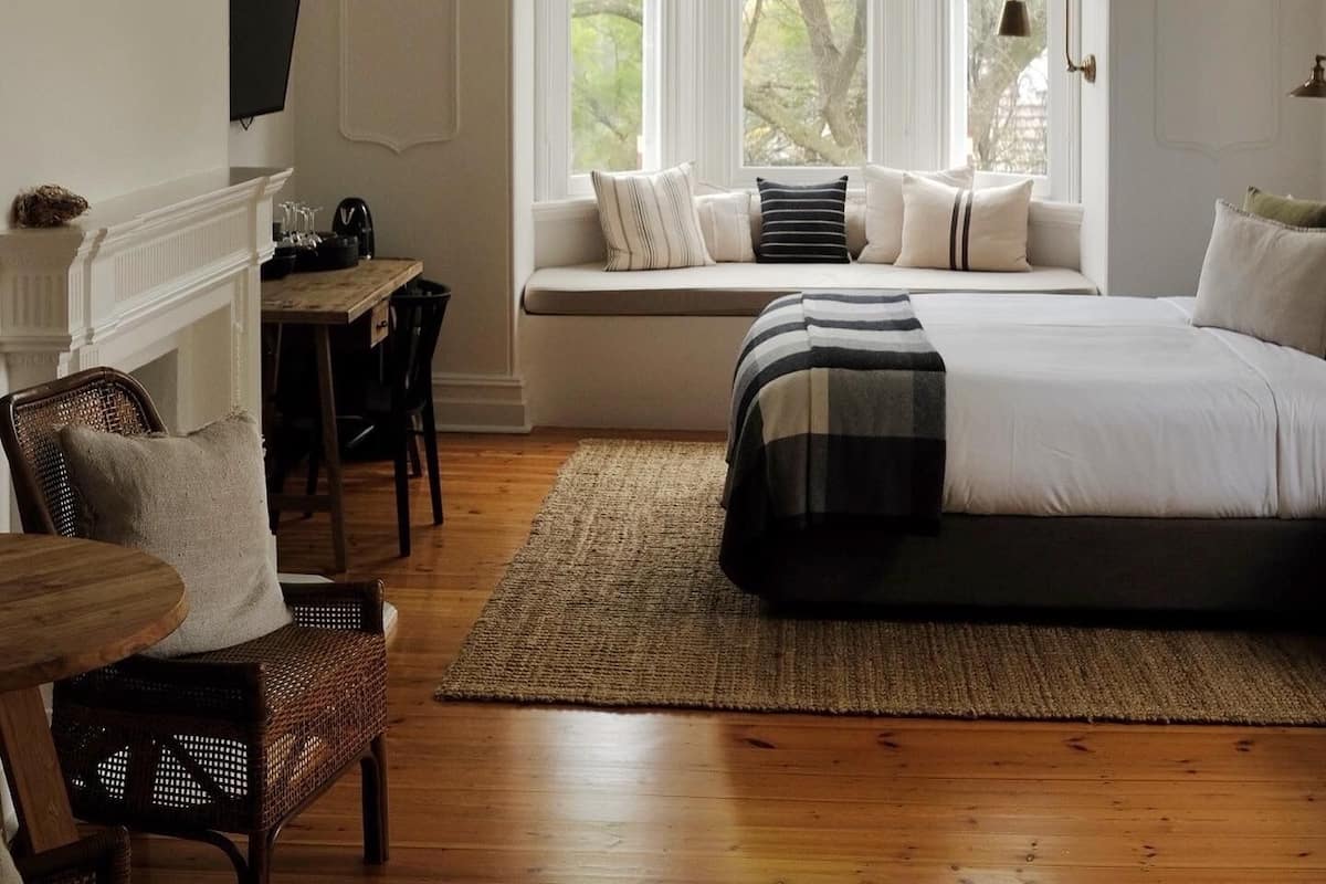 A bedroom with a large bed, a window seat with pillows, a fireplace, and a deer head mounted on the wall.