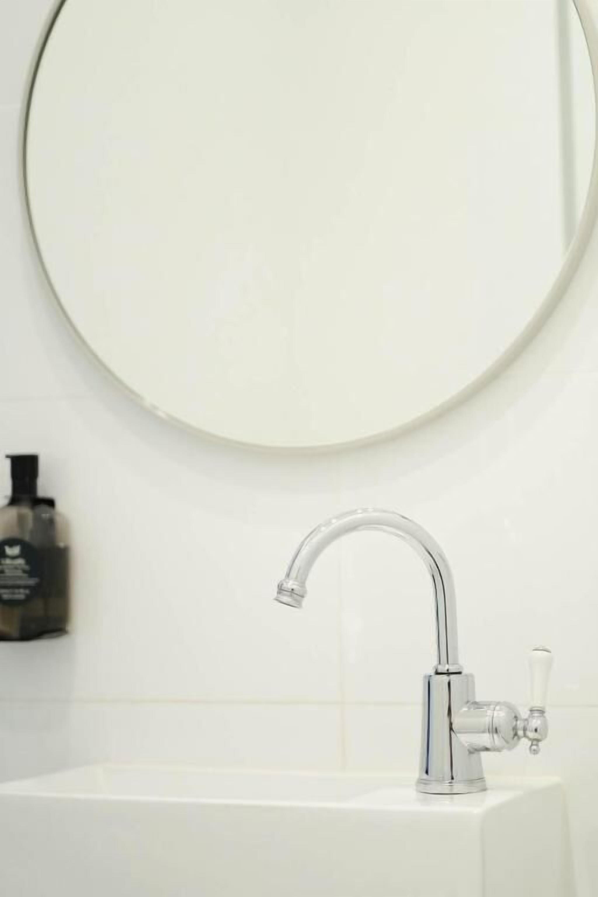 Een badkamer met een witte wastafel, een chromen kraan en een ronde spiegel.