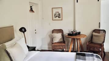 Quarto com cama, duas cadeiras de vime, uma mesinha redonda com um conjunto de chá e um quadro na parede.