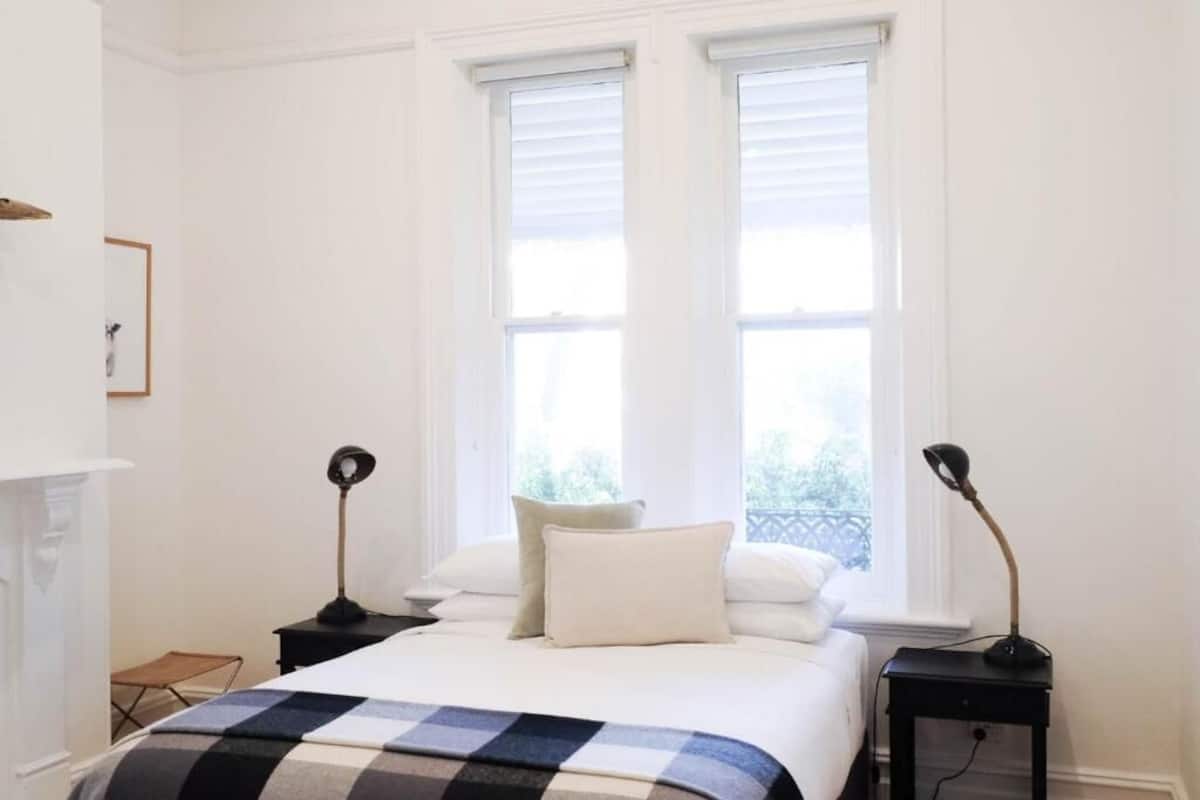 A bedroom with a bed, two bedside tables, a window, and a view of greenery outside.