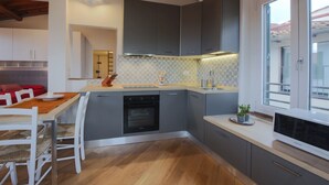 A modern kitchen with grey cabinets, a built-in oven, and a dining area with a wooden table and chairs.