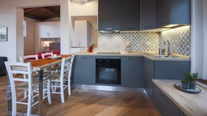 A modern kitchen with grey cabinets, a built-in oven, and a dining area with white chairs.