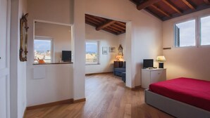 A bedroom with a bed, a TV, a desk with a lamp, a mirror, and a window.