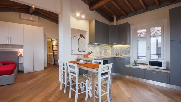 A modern kitchen with white cabinets, a wooden dining table, and a red sofa in the adjacent room.