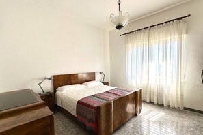 A bedroom with a wooden bed, a desk, a lamp, and a chandelier.