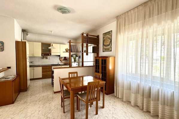 A compact kitchen with a dining area, wooden cabinets, and a window with sheer curtains.