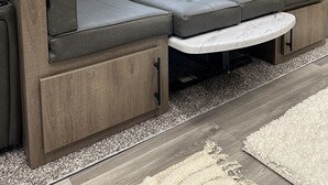A modern RV interior with a sectional sofa, a small table, and two windows providing views of the outside. - Beach Haven (Sekiu)