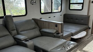 A modern RV interior with a sectional sofa, a dining table, and a small kitchen area. - Beach Haven (Sekiu)