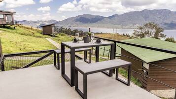 Una terraza con mesa y bancos con vistas a un lago y montañas.
