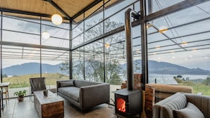 A modern living room with a large glass wall, a fireplace, and a sofa. - Fuga Neusa (Tausa)