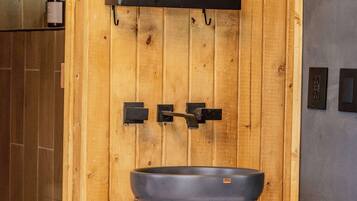 A bathroom with a wooden wall, a black sink, and a shelf with toiletries.