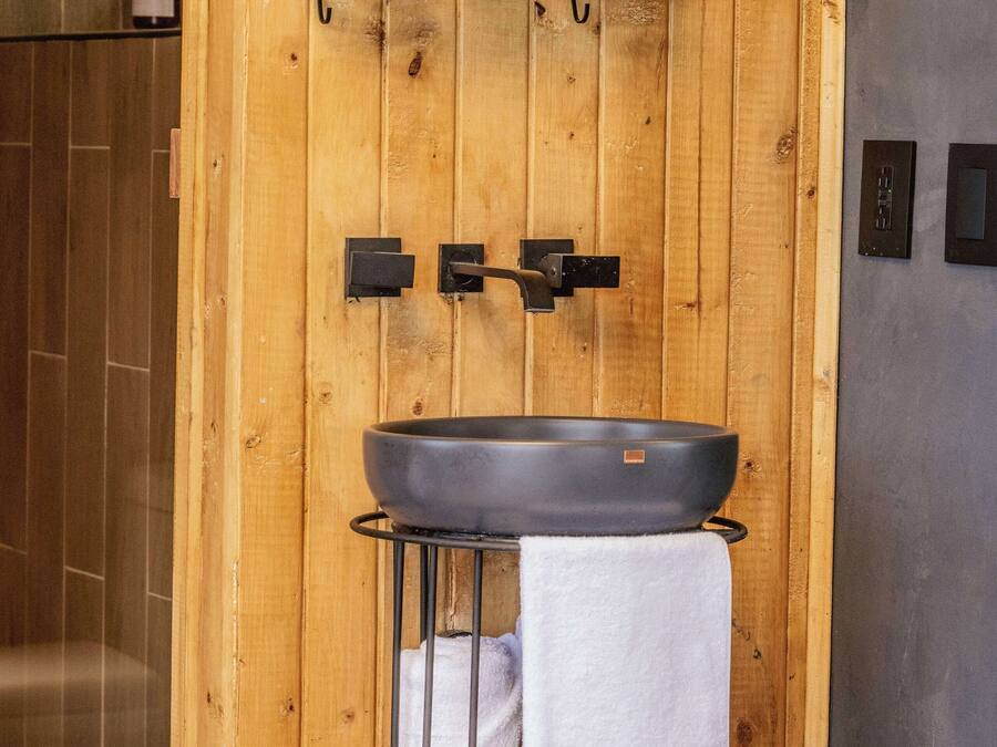 A bathroom with a wooden wall, a black sink, and a shelf with toiletries.