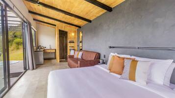 Een moderne hotelkamer met een groot bed, een bank, een kitchenette en uitzicht door grote ramen.
