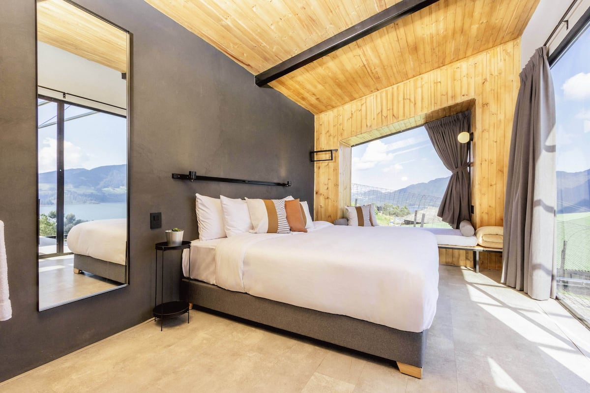 A modern bedroom with a large bed, a mirror, and a view of the mountains.