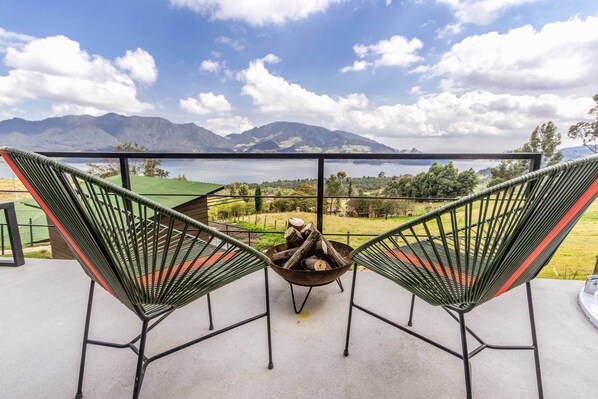 Two green metal chairs with red accents facing a fire pit on a balcony overlooking a lake and mountains. - Fuga Neusa (Tausa)