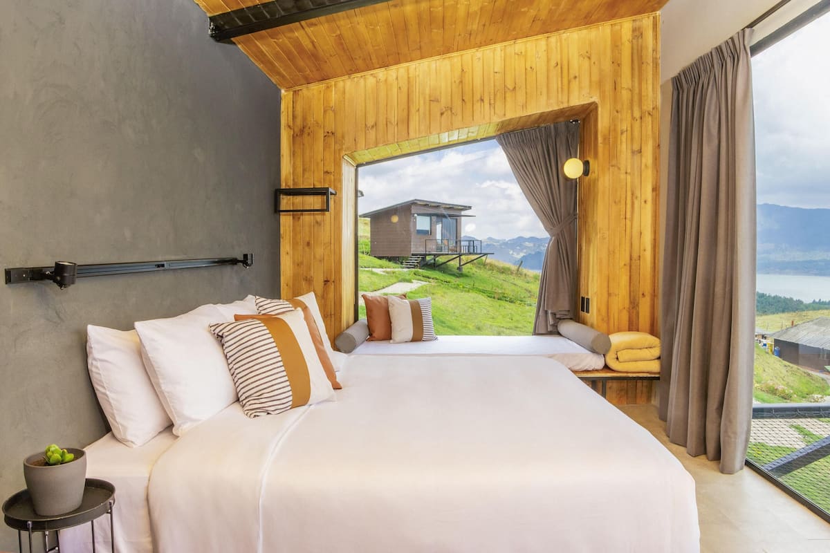 A bedroom with a large bed, wooden walls, a window with curtains, and a view of a small building outside.