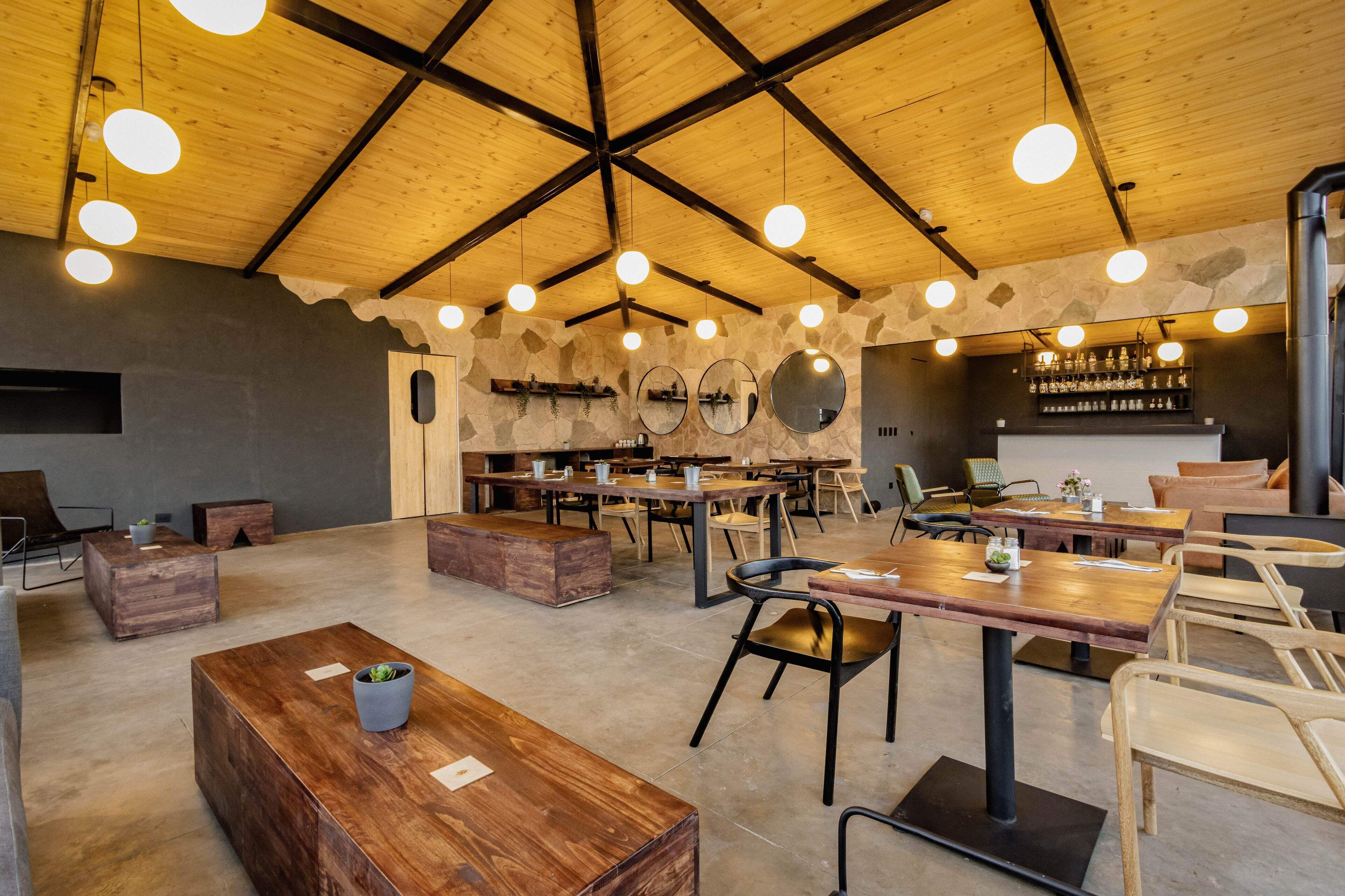A spacious indoor area with wooden tables and chairs, a stone wall with mirrors, and hanging lights.