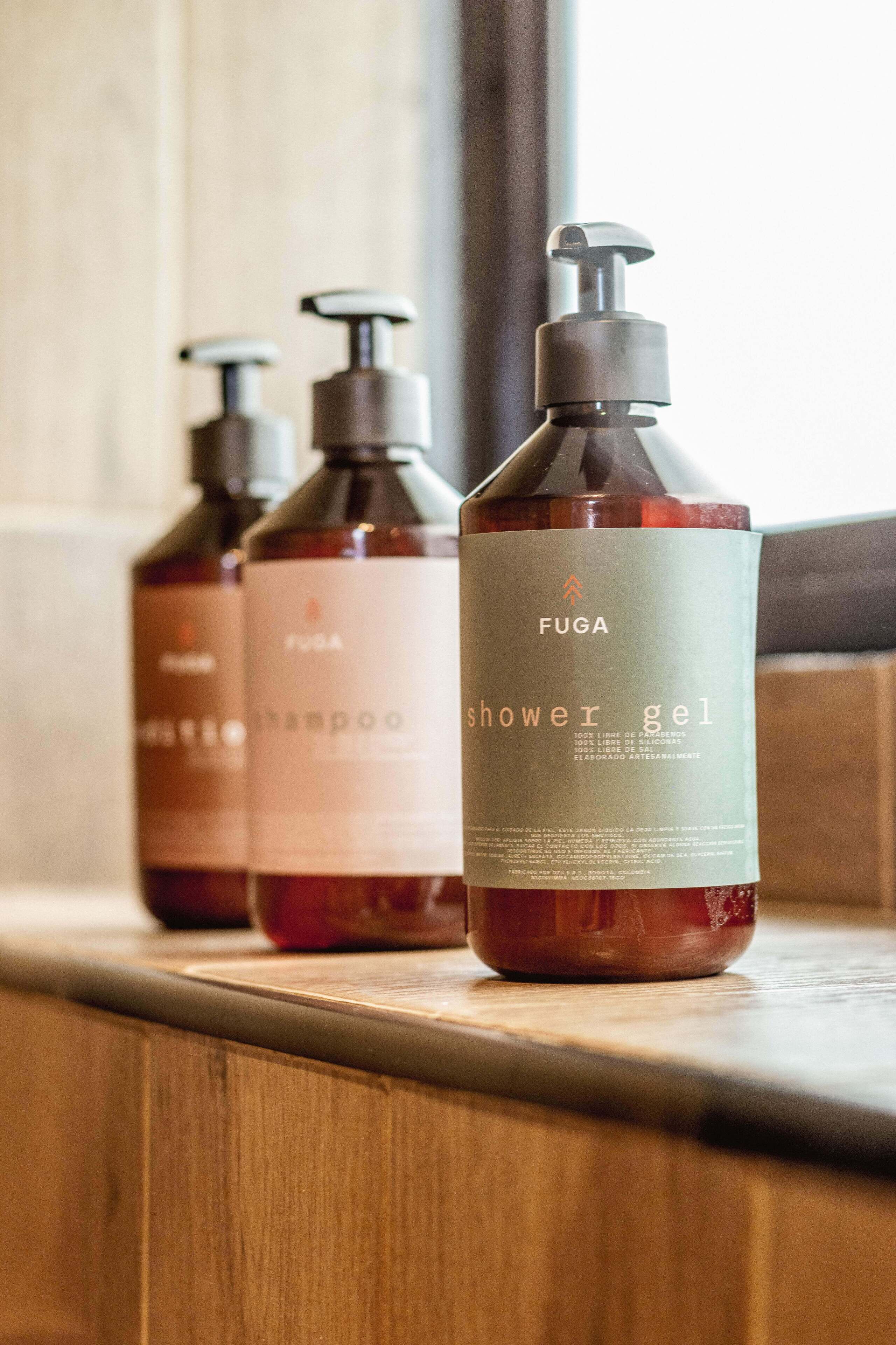 Trois bouteilles de gel douche FUGA sont posées sur une étagère en bois.
