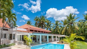 Une maison à deux étages avec une piscine, un espace salon extérieur et des palmiers.