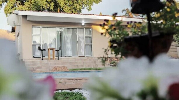 Una casa moderna con piscina, dos sillas afuera y un jardín en primer plano.