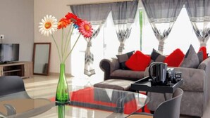 Una sala de estar moderna con una mesa de centro de vidrio, un sofá gris con cojines rojos, y un televisor al fondo.