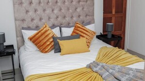 Una cama bien hecha con un cabecero capitonado, una manta amarilla y almohadas estampadas.