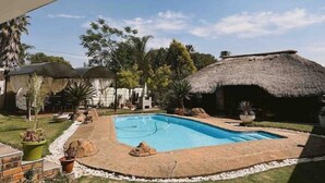 Un patio trasero con piscina, una estructura de techo de paja y plantas en macetas.