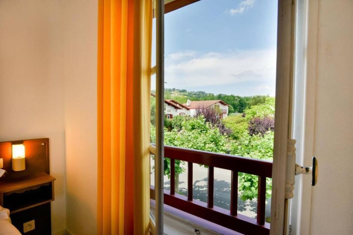 A room with a view of a house and greenery through an open door.
