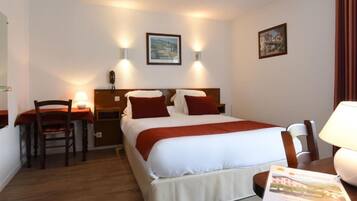 Una habitación de hotel con una cama, mesitas de noche, un escritorio, una silla y una lámpara.