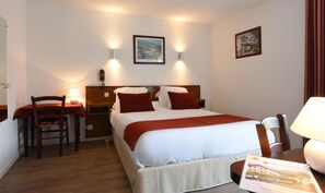 A hotel room with a bed, bedside tables, a desk, a chair, and a lamp. - Logis Hotel Baratxartea (Sare)