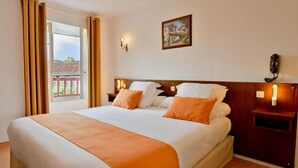 A hotel room with a bed, a nightstand, a wall-mounted lamp, and a window with curtains. - Logis Hotel Baratxartea (Sare)