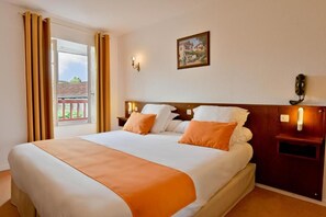 A hotel room with a bed, a nightstand, a wall-mounted lamp, and a window with curtains. - Logis Hotel Baratxartea (Sare)