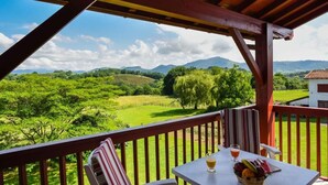 A balcony with a table, chairs, and a view of green fields and mountains. - Logis Hotel Baratxartea (Sare)