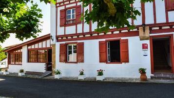Un edificio tradicional de entramado de madera con contraventanas rojas, una entrada visible y plantas en macetas en el suelo.