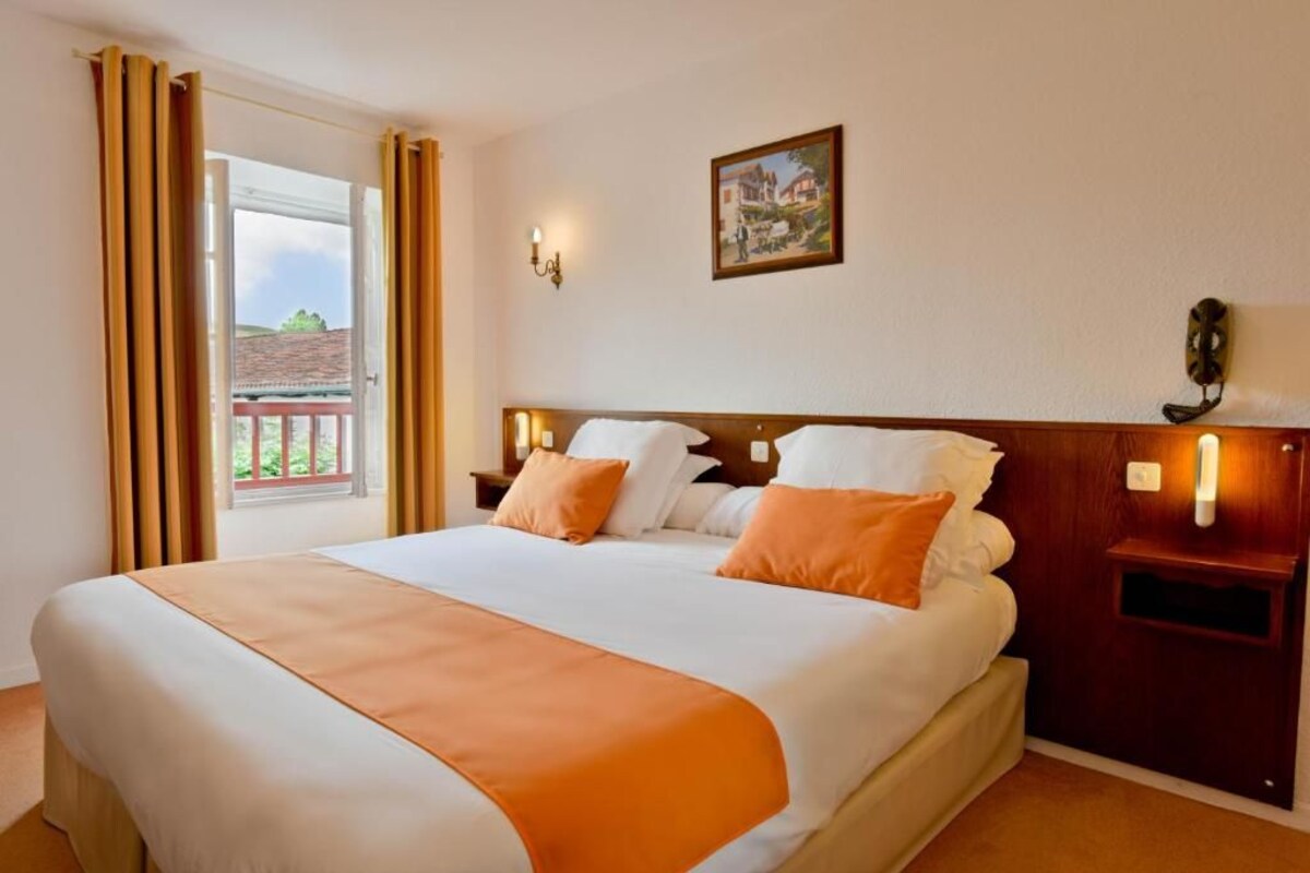 A hotel room with a bed, a nightstand, a wall-mounted lamp, and a window with curtains.