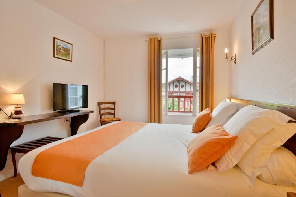Una habitación de hotel con una cama, un escritorio con televisor, una silla y una ventana con cortinas.