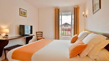 Una habitación de hotel con una cama, un escritorio con televisor, una silla y una ventana con cortinas.