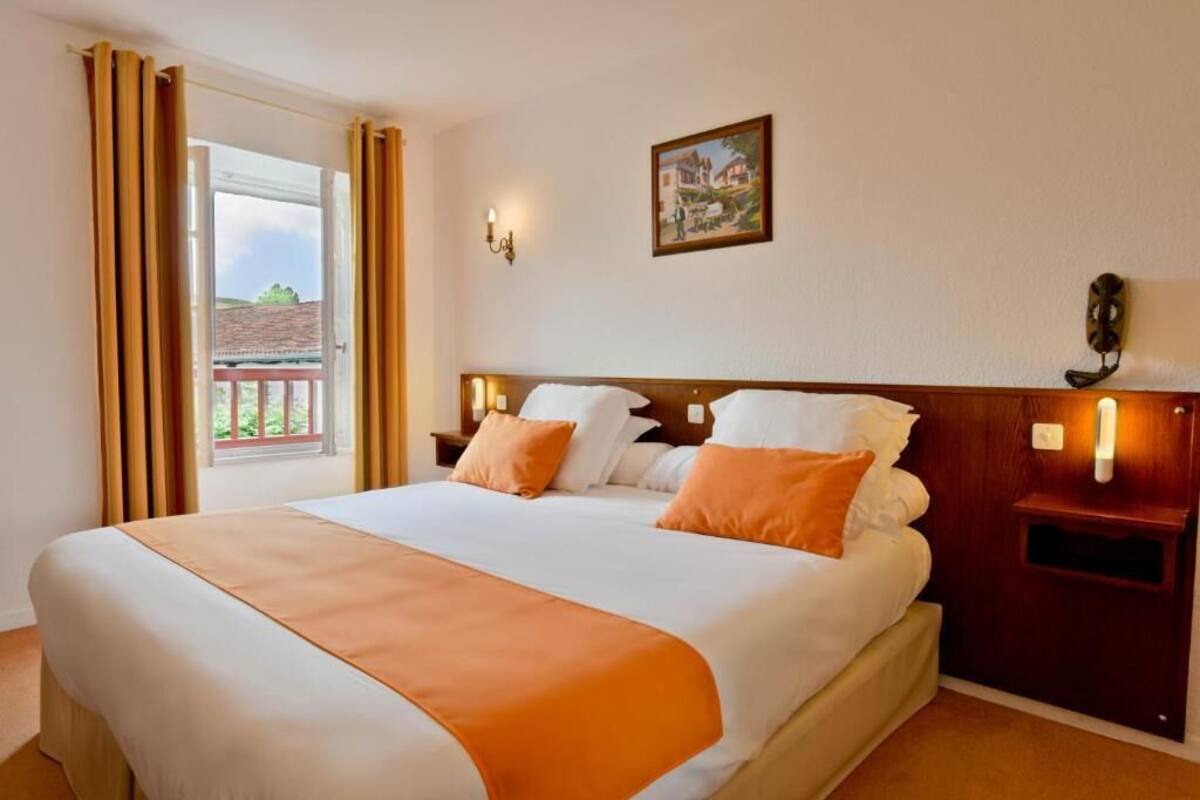 A hotel room with a bed, a nightstand, a wall-mounted lamp, and a window with curtains.